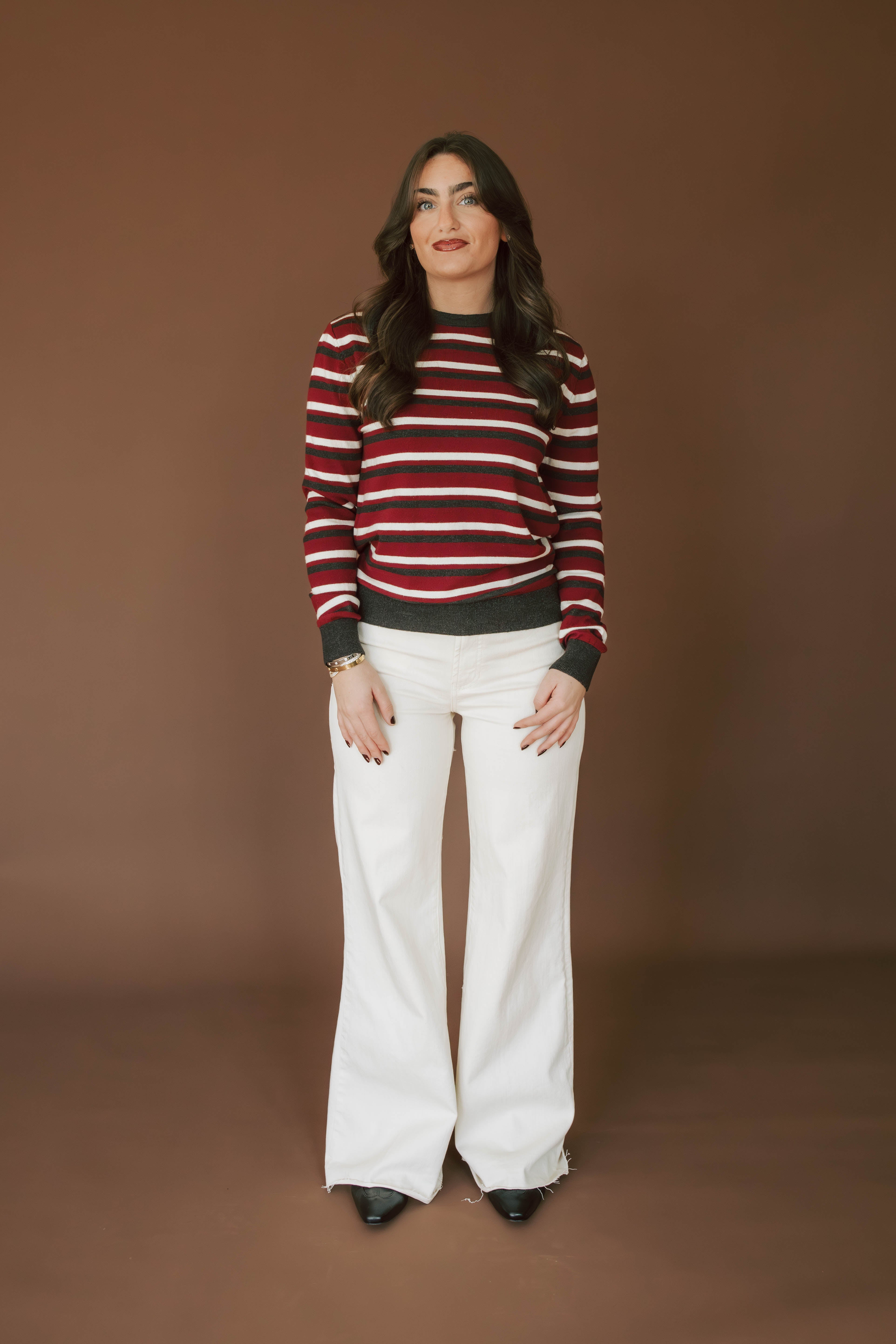 Woman wearing a red and white striped sweater and white pants against a brown background