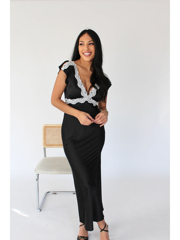 Black satin maxi dress with V-neck and fly-away cap sleeves - Elegant and feminine, featuring white lace detail on the V-neck and sleeves,  a timeless wedding guest dress.