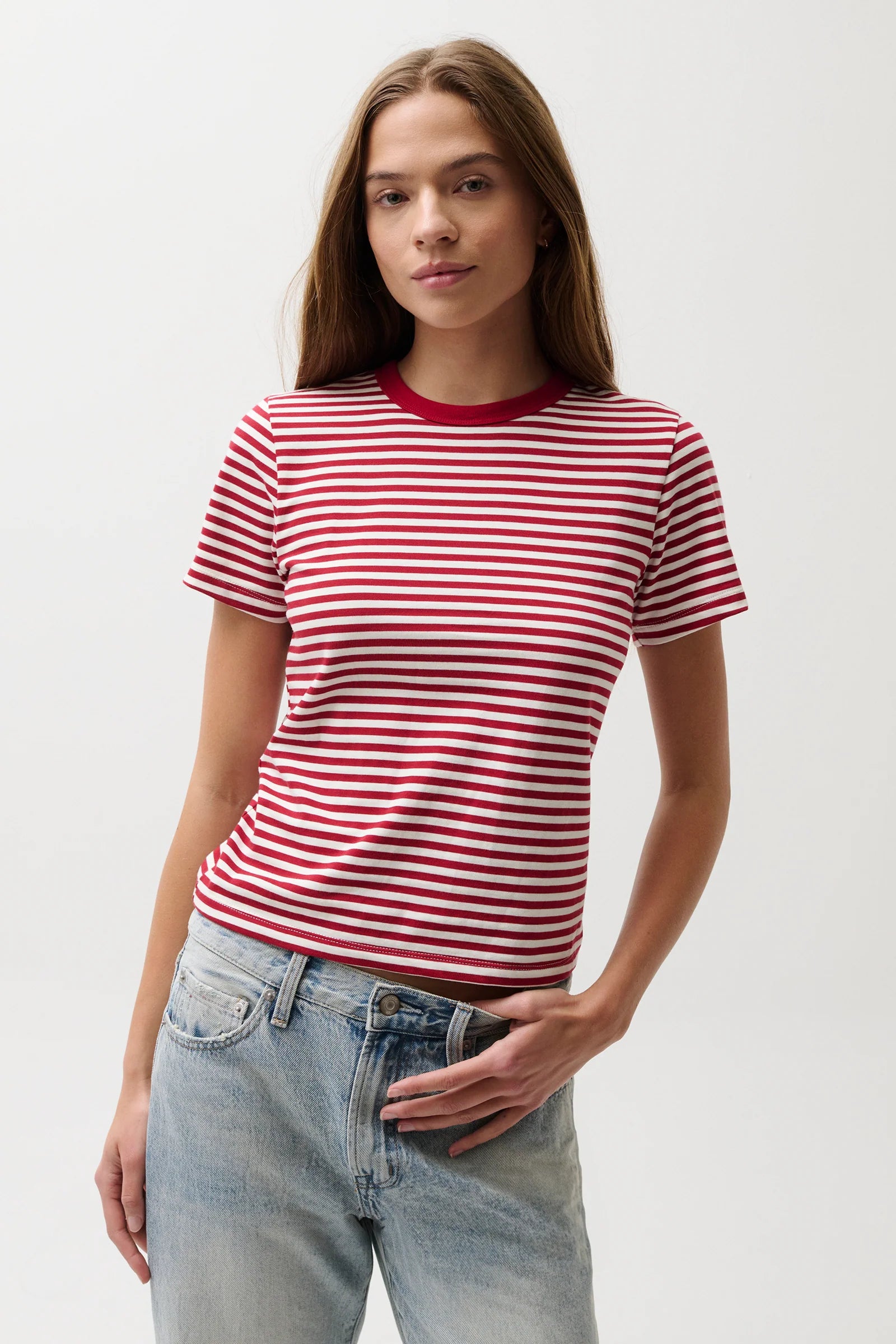 Woman wearing a red and white striped shirt with blue jeans on a plain background